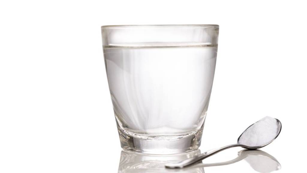 A clear glass filled with water next to a silver spoon with a small amount of salt.