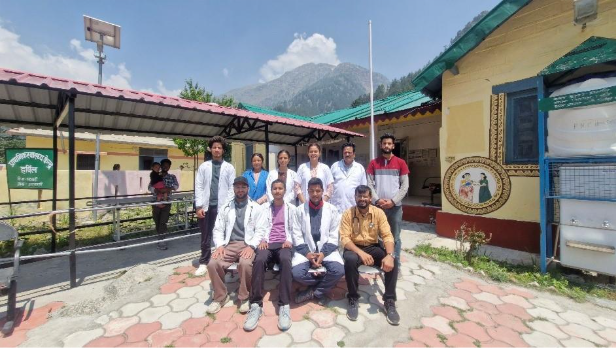 Group of healthcare professionals in white coats posing outside a clinic with mountains in the background.
