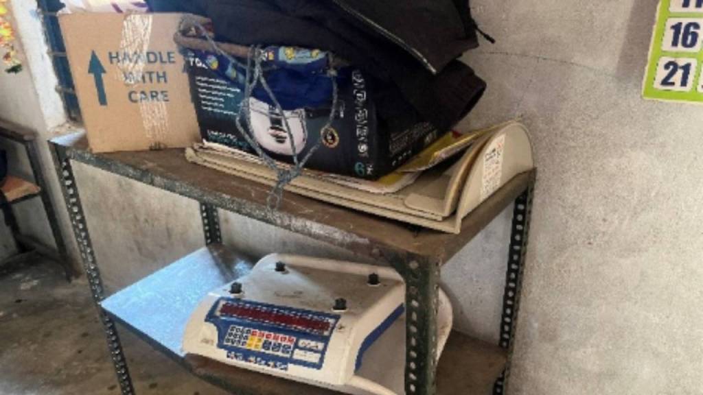 A shelf holding various items, including a cardboard box labeled 'HANDLE WITH CARE,' several bags, and a digital scale used for weighing.