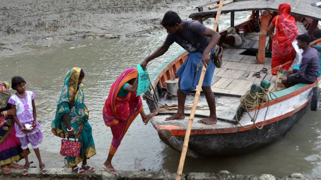 A group of people wearing colorful traditional clothing boarding a boat by the water. One person is assisting another in stepping onto the boat while others wait nearby.
