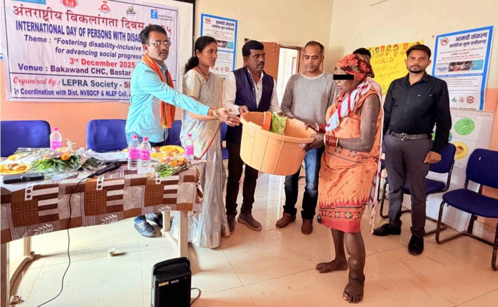 A group of people is participating in a ceremony for the International Day of Persons with Disabilities, with one individual receiving a basket of items while others look on.