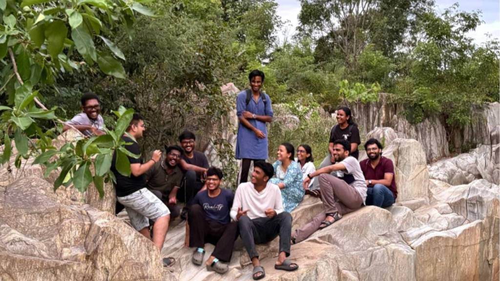 A group of eleven people smiling and posing together on rocky terrain surrounded by greenery.