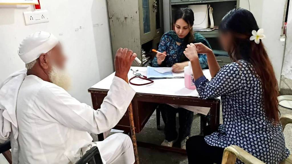 A healthcare professional sitting at a table with a patient, while another person engages in conversation. The setting appears to be a clinic or office.